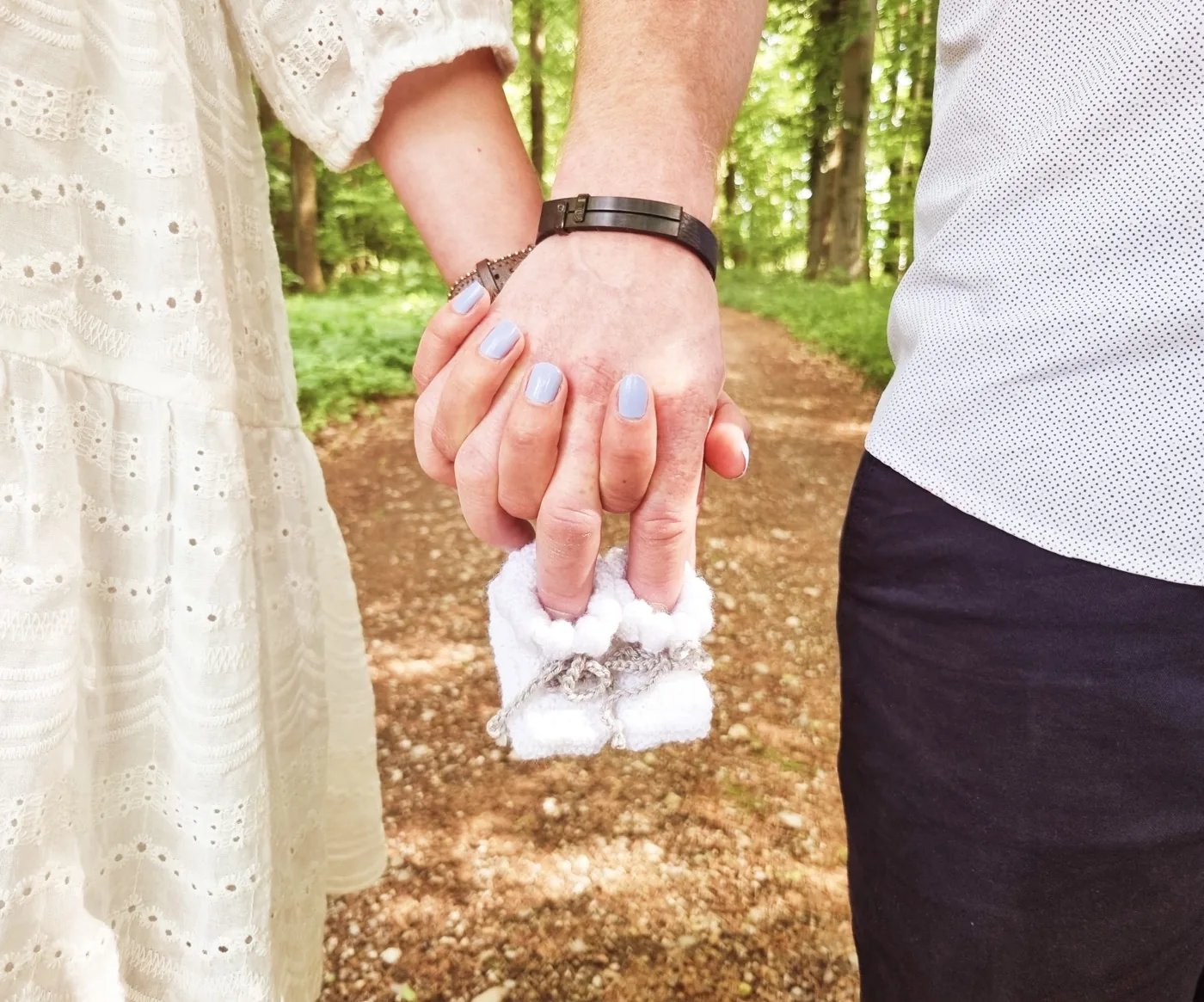 Werdende Eltern halten im Wald Händchen, dazwischen winzige Babyschuhe — sanfte Begleitung in der Schwangerschaft